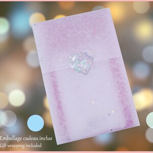 May include: A lavender gift envelope with a glittery heart-shaped sticker. The envelope has a textured appearance and is decorated with small, sparkling accents. Text on the bottom reads "Gift wrapping included."