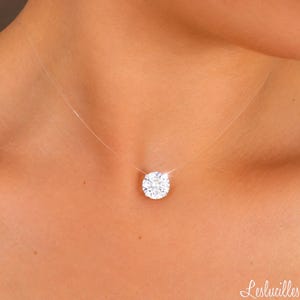 May include: A clear, thin nylon fishing line necklace featuring a single, round, brilliant-cut white gemstone pendant. The stone is set in a simple, minimalist metal prong setting, creating a floating effect against the skin. The text Leslucilles is visible.