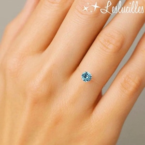 May include: A delicate ring featuring a round, light blue gemstone. The ring appears to be held by a nearly invisible band, creating a floating effect. The image includes the text "Leslucilles" in the upper right corner.