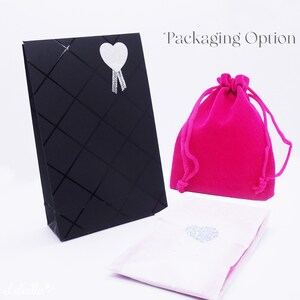 May include: An assortment of packaging options, including a black gift bag with a diamond pattern and a silver heart sticker, a bright pink velvet drawstring bag, and a white pouch with a heart sticker. The text "Packaging Option" is visible.