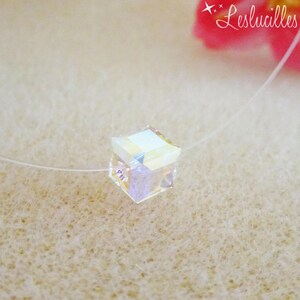 Puede incluir: Collar con colgante de cubo transparente e iridiscente. El cubo está suspendido de un hilo casi invisible. El fondo es de un color suave y neutro, con el texto "Leslucilles" en la esquina superior derecha.