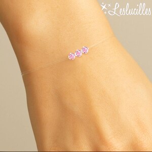 May include: A delicate bracelet featuring three pink gemstones strung on a nearly invisible cord. The bracelet is shown on a wrist, with the gemstones evenly spaced. The brand name "Leslucilles" is in the upper right corner.