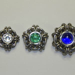May include: Three silver metal jewellery pieces with different coloured gemstones. The first piece has a clear gemstone, the second has a green gemstone, and the third has a blue gemstone.