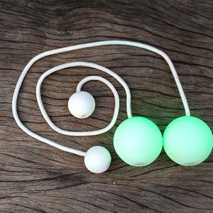 Op de afbeelding: Een set glow-in-the-dark jongleerballen met een wit touw. De ballen zijn groen en wit.