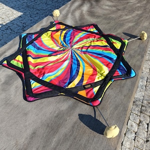 May include: A colorful, star-shaped, fabric play mat with a swirling pattern of red, yellow, blue, and green. The mat has black trim and is attached to five yellow balls by black strings.