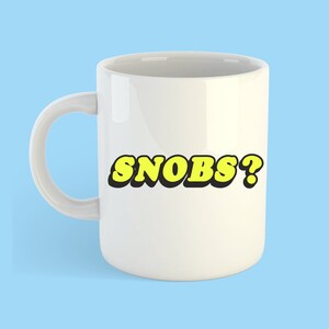 May include: White ceramic mug with a yellow and black graphic that says "SNOBS?"