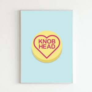 May include: A yellow heart-shaped sweet with the text "KNOB HEAD" in pink lettering. The sweet is on a light blue background.