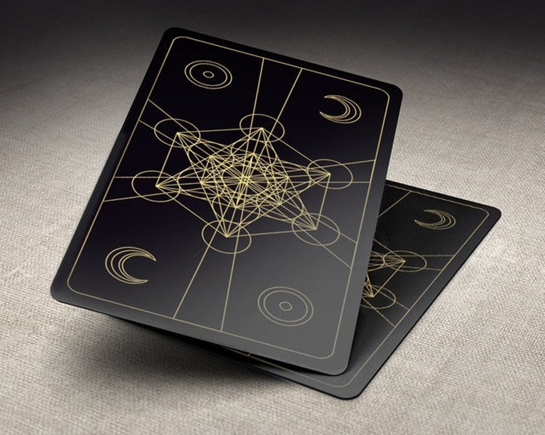 May include: Two black playing cards with gold geometric designs. The cards feature a complex, intricate pattern of overlapping circles and lines, creating a visually striking effect.