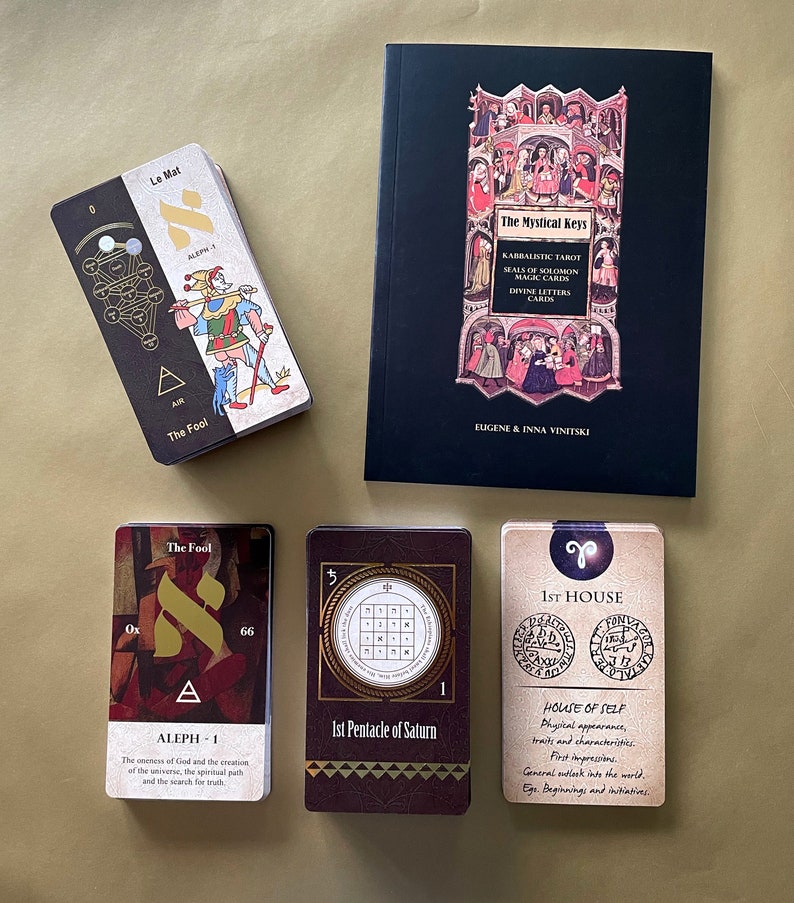 May include: A set of tarot cards with a black and gold design. The cards feature illustrations of a jester, a pentagram, and a zodiac symbol. The cards are part of a larger set called "The Mystical Keys: Kabbalistic Tarot, Seals of Solomon, Magic Cards, Divine Letters Cards".