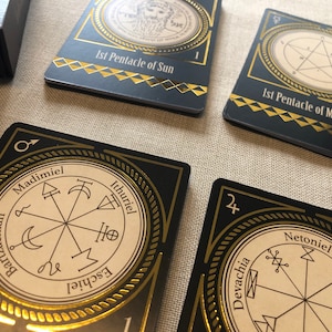 May include: Four black cards with gold trim and a white background. Each card features a circle with a symbol and text inside. The text on the cards includes "1st Pentacle of Sun", "1st Pentacle of Mercury", "Madmiel", "Ithuriel", "Devachia", "Netoniel", "Bartzachiah", "Eschiel", "Parasi".