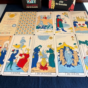 Peut inclure: Un &eacute;talement de cartes de tarot du jeu Tarot de Marseille de la Nouvelle Incarnation. Les cartes sont dispos&eacute;es en rang&eacute;e sur une surface bleue. Les cartes montrent diverses images, notamment un homme avec une &eacute;p&eacute;e, une femme avec une coupe et un homme avec une pi&egrave;ce de monnaie.