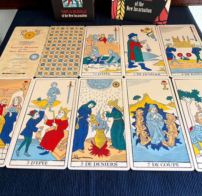 Peut inclure: Un &eacute;talement de cartes de tarot du jeu Tarot de Marseille de la Nouvelle Incarnation. Les cartes sont dispos&eacute;es en rang&eacute;e sur une surface bleue. Les cartes montrent diverses images, notamment un homme avec une &eacute;p&eacute;e, une femme avec une coupe et un homme avec une pi&egrave;ce de monnaie.