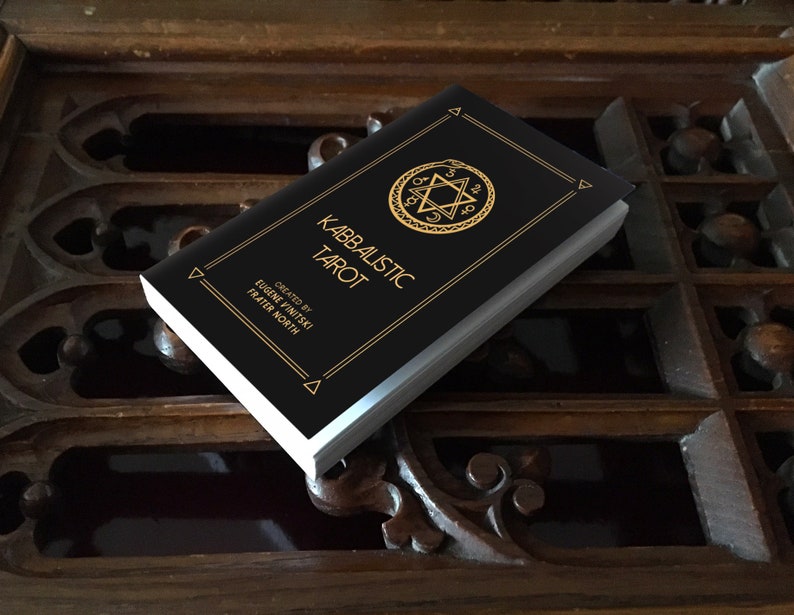 May include: A black book with gold lettering titled "Kabbalistic Tarot" by Eugene Vinitski, Frater North. The book features a gold star of David with a snake wrapped around it.