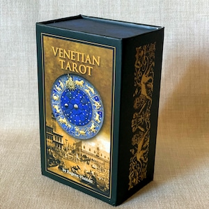 May include: A black box with gold accents and the text "Venetian Tarot" on the front. The box features a blue and gold illustration of a zodiac wheel with a cityscape in the background. The text "by Eugene Vinitski" is at the bottom of the box.