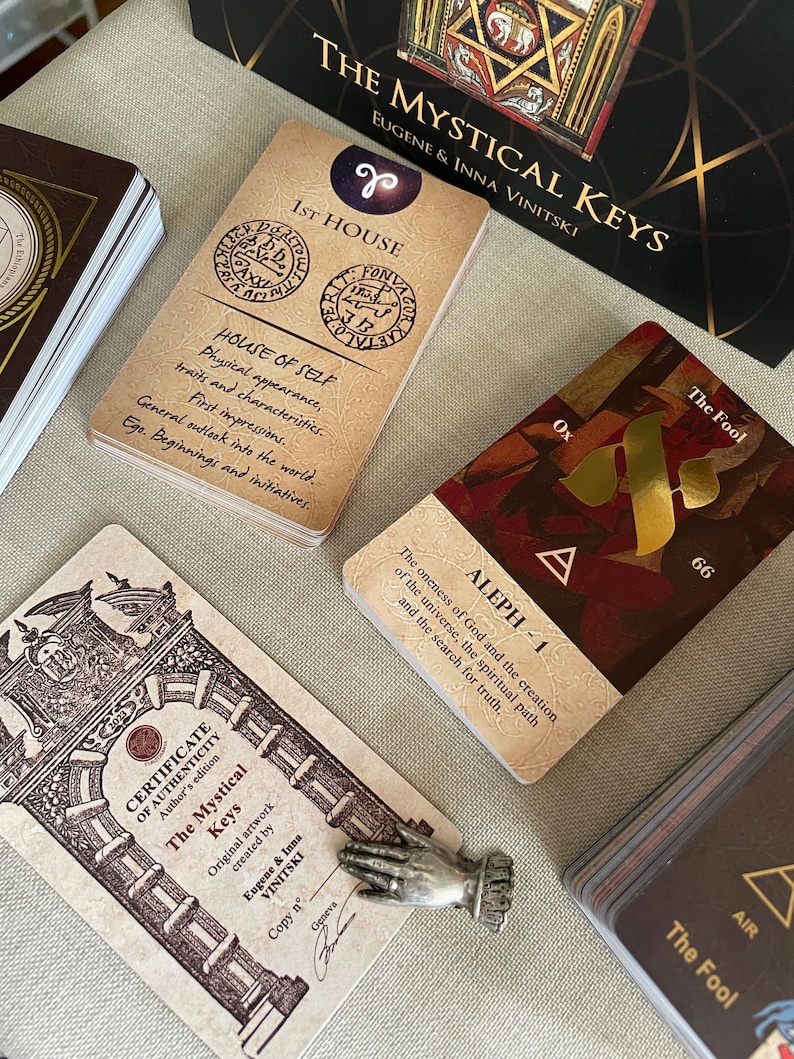 May include: A set of tarot cards with a certificate of authenticity. The cards feature a gold and red design with the text "The Mystical Keys" and "Aleph - 1".