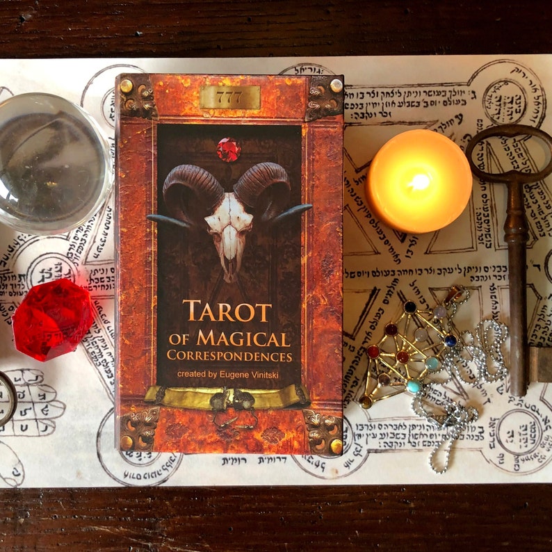 May include: A tarot deck box with a brown leather cover and gold accents. The box has the title "Tarot of Magical Correspondences" and the text "created by Eugene Vinitski".