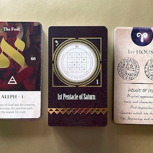 May include: Three tarot cards with gold accents. The first card is The Fool, with the Hebrew letter Aleph and the text "The oneness of God and the creation of the universe, the spiritual path and the search for truth." The second card is the 1st Pentacle of Saturn, with a Hebrew letter grid and the number 1. The third card is the 1st House, with the astrological symbol for Aries and the text "House of Self, Physical appearance, traits and characteristics. First impressions. General outlook into the world. Ege. Beginnings and initiatives."