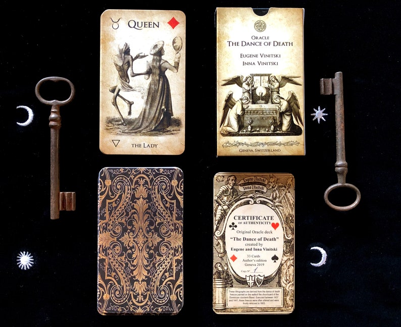 May include: An oracle card deck titled "The Dance of Death" with illustrations and text. The deck includes cards, a box, and a certificate of authenticity. Two antique keys and decorative celestial shapes are also present.