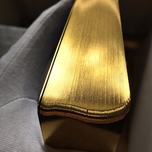 May include: A close-up of a stack of gold-colored playing cards. The cards are arranged in a neat, even stack, and the edges of the cards are visible.
