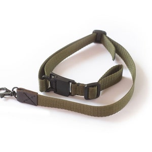 Peut inclure: Une sangle de caméra verte avec une boucle noire réglable et une boucle en cuir marron avec un fermoir métallique.