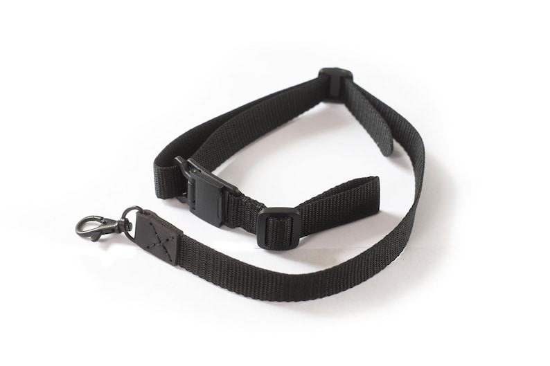 May include: A black camera strap with a leather accent and a metal clip. The strap has a buckle for adjusting the length.