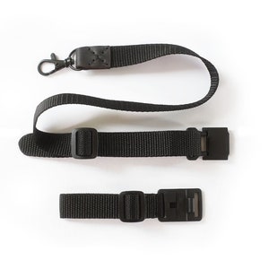 May include: A black camera strap with a metal clip and two adjustable buckles.