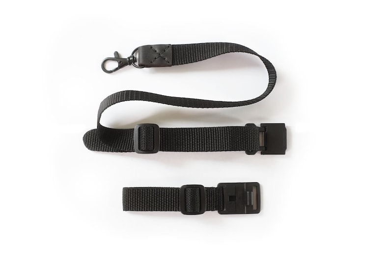 May include: A black camera strap with a metal clip and two adjustable buckles.