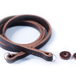 May include: A brown leather camera strap with the text "Replants" and "replants.com" embossed on it. The strap has two metal rings and two brown leather rings.