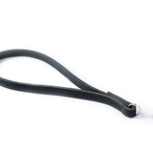 Pode incluir: Uma correia de câmera de couro preto com um anel de metal e um botão de borracha preto.