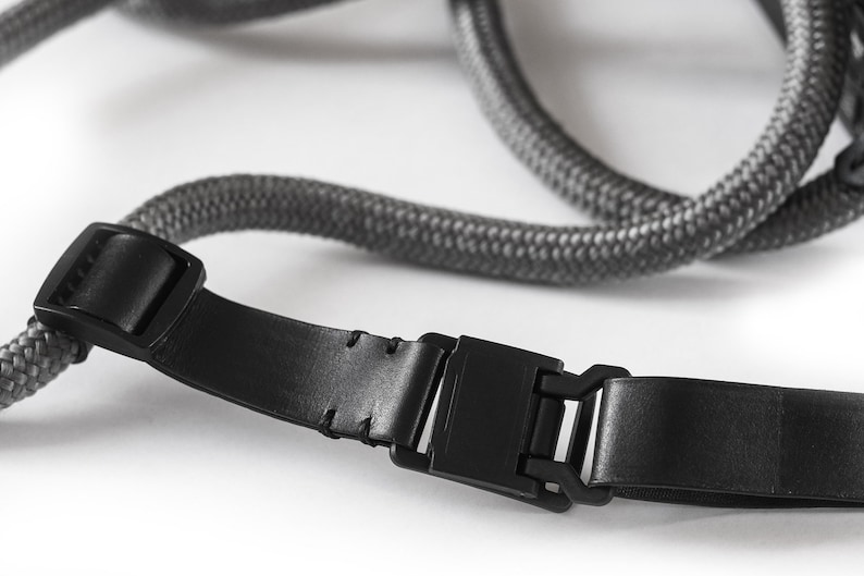 May include: A black leather camera strap with a grey rope and a black plastic buckle.