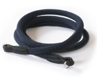 May include: A dark blue camera strap made of woven fabric with black leather ends and a silver metal ring.