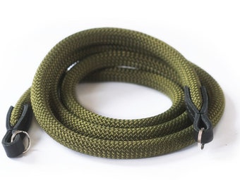 May include: A green camera strap made of braided rope with black leather ends and metal rings.