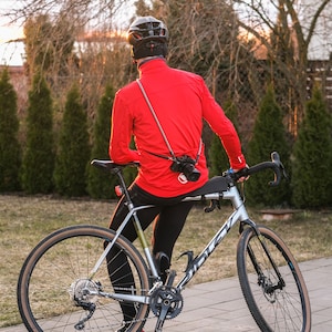 May include: A person wearing a red jacket and a black helmet is sitting on a silver and black bicycle. The bicycle has brown handlebar tape and brown tyres. The person is looking away from the camera.
