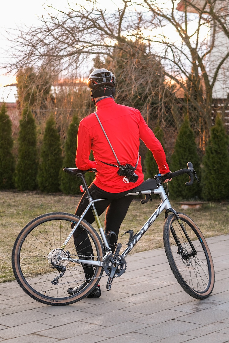 May include: A person wearing a red jacket and a black helmet is sitting on a silver and black bicycle. The bicycle has brown handlebar tape and brown tyres. The person is looking away from the camera.
