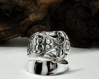 Op de afbeelding: Een zilverkleurige lepelring met een ingewikkeld in reliëf gemaakt bloemmotief op de bovenste band en een gladde, gepolijste afwerking op de onderste band. De tekst HALO SPOON RINGS is zichtbaar bovenaan de afbeelding boven de ring.