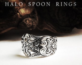 Op de afbeelding: Een zilverkleurige metalen ring gemaakt van een lepelsteel, voorzien van ingewikkelde reliëfkrullen en bloemmotieven. De tekst HALO SPOON RINGS staat in witte hoofdletters boven de ring tegen een donkere, getextureerde achtergrond.