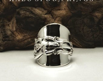 Op de afbeelding: Een zilverkleurige lepelring met een gepolijst, reflecterend oppervlak en een ingewikkeld, in reliëf gemaakt krulpatroon langs de middelste band. De tekst HALO SPOON RINGS staat in witte hoofdletters boven de metalen ring.