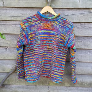May include: A colourful striped jumper with a high neck and long sleeves. The jumper is made from a soft, textured yarn and features a variety of colours, including blue, red, yellow, and green.