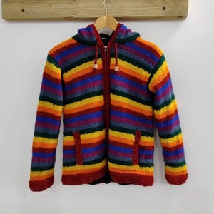 Könnte beinhalten: Ein bunter gestreifter Kapuzenpullover mit Reißverschluss und zwei Taschen. Der Pullover ist aus weichem, gestricktem Stoff und hat ein Regenbogen-Farbmuster.