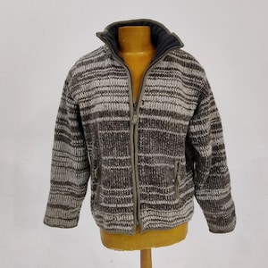 May include: A full-zip, brown and white striped knit jacket with a high collar. The jacket has two front pockets and a dark blue lining inside the collar. The jacket is displayed on a wooden mannequin.