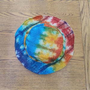 May include: A tie-dye bucket hat made of woven fabric. The hat is blue, yellow, red, and green.