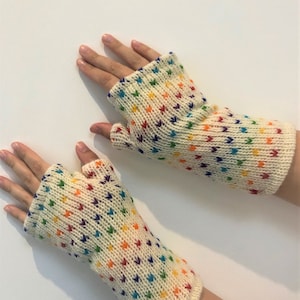 Peut inclure: Une paire de mitaines blanches avec un motif arc-en-ciel. Les mitaines sont tricotées avec un petit motif de cœur répétitif.