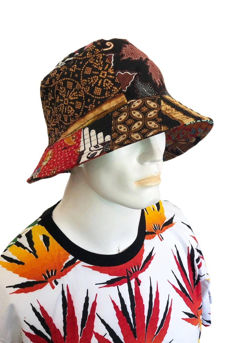Op de afbeelding: Een zwarte bucket hat met een patchwork ontwerp met verschillende patronen in tinten bruin, rood en wit. De hoed is gemaakt van katoenen stof en heeft een brede rand.