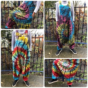 Op de afbeelding: Een tie-dye overall met een draaiende print in tinten blauw, rood, geel en zwart. De overall heeft een grote zak aan de voorkant en verstelbare banden.