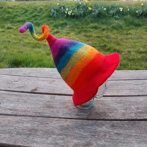 May include: A rainbow-coloured felt hat with a long, curled brim. The hat is made of wool and has a bright, colourful design.
