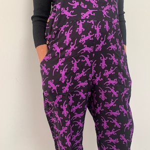 May include: Black overalls with a purple gecko print. The overalls have a wide leg and a relaxed fit.