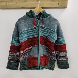 May include: A multi-coloured striped knitted hooded jacket with a zip closure. The jacket has a patchwork design with different coloured stripes and a large pocket on the front.