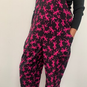 May include: Black overalls with a pink lizard print. The overalls have a wide leg and a relaxed fit.