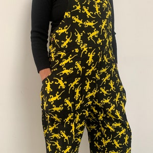 May include: Black overalls with a yellow lizard print. The overalls have adjustable straps and large pockets.
