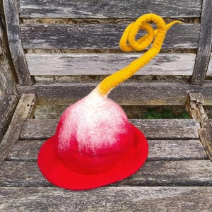 May include: A red and white felt hat with a yellow felt stem. The hat is sitting on a wooden surface.
